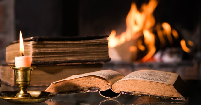 Open Bible in front of a candle and a bonfire