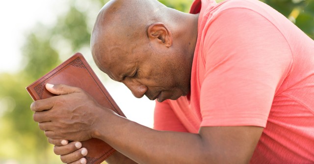Man with Bible bowing head in prayer