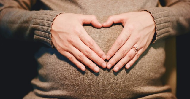 A woman making a heart with her hands over her pregnant belly