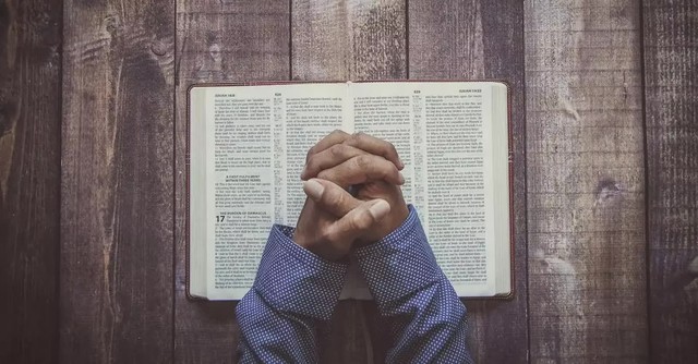 Hands folded in prayer over a Bible
