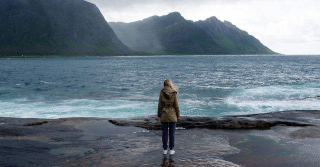 Woman standing by the sea with mountains in the distance