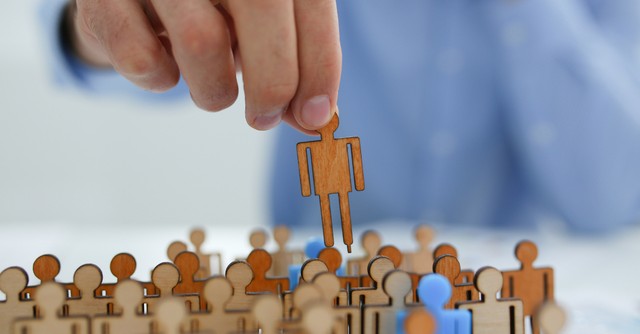 Hand picking a wooden figure out of a group