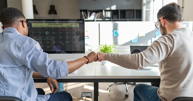 Two men fist-bump at work