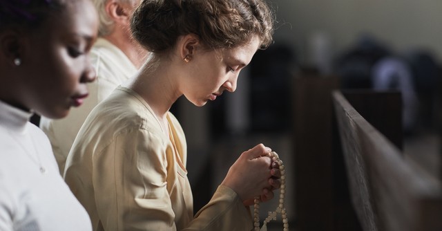Young catholic woman praying with a rosary