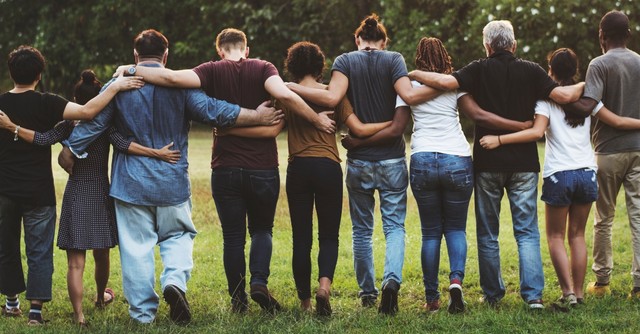 A group of people standing with their arms around each other, united