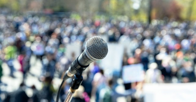 Microphone in front of a blurry crowd of people, at a rally