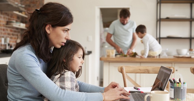 Busy mom working at home on laptop with family