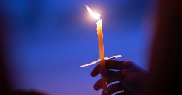 A person holding a single lit taper candle at Christmas