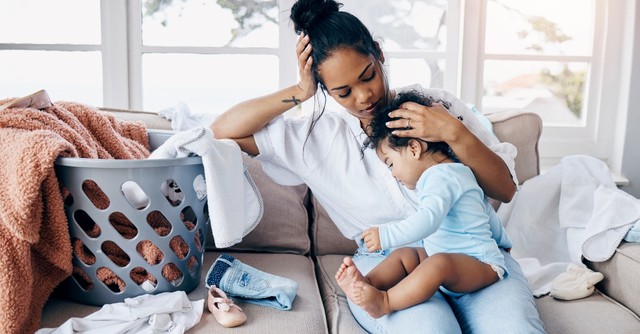 Tired, overwhelmed mom sitting on the couch with her baby and laundry