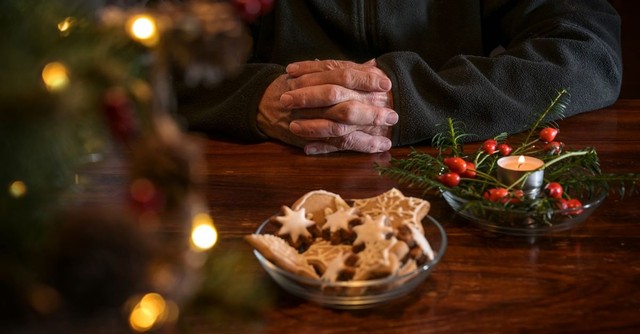 An elderly person with hands folded in prayer, surrounded by Christmas decorations