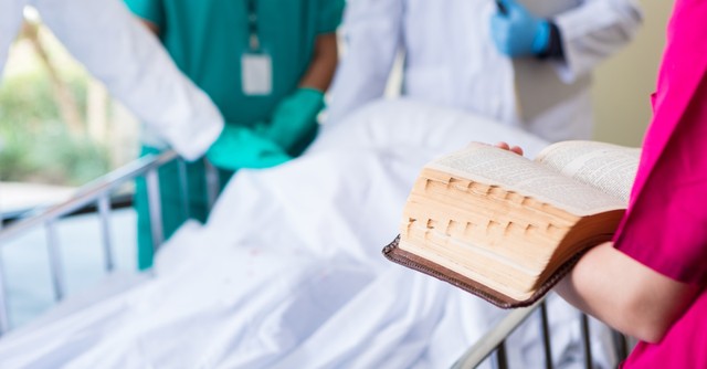 Nurse reading a Bible to someone in a hospital bed