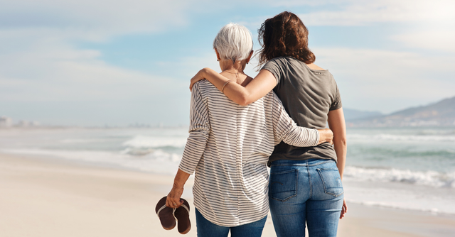 Older woman and younger woman walking arm in arm on the beach