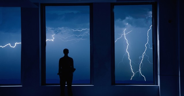 Man standing at a window, watching a lightning storm