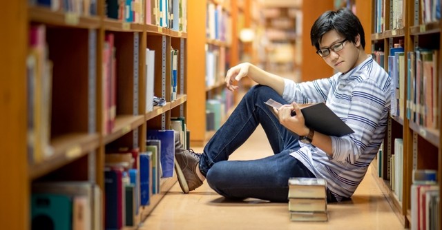 Student sitting in a library reading a stack of books