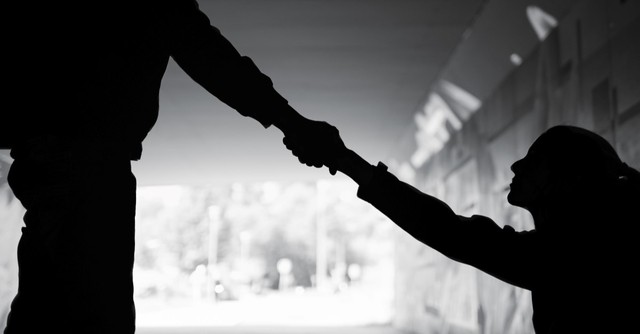 Silhouette of a man reaching a hand down to help a woman
