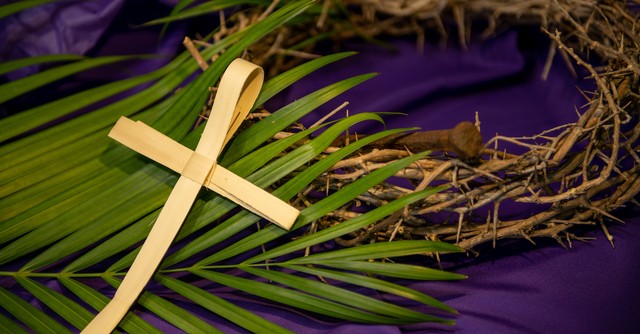 Palm branches, a palm cross, and a crown of thorns on a purple cloth