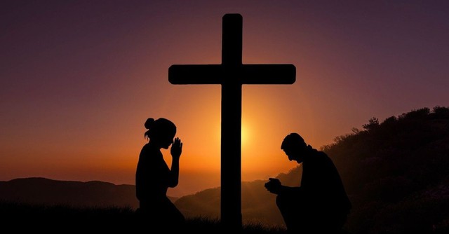 People praying by the cross at sunset