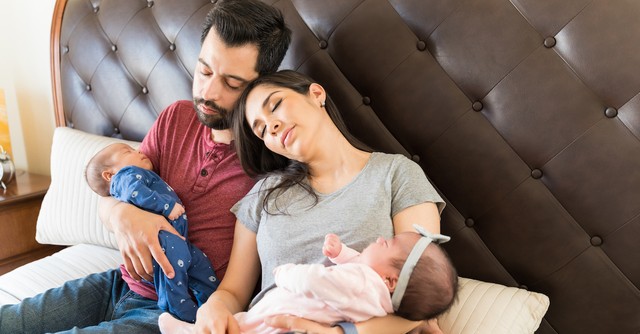 Exhausted parents with newborn twins on bed sleeping