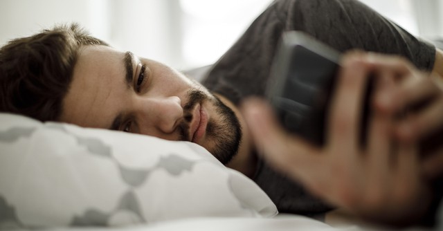 Man checking cell phone in bed