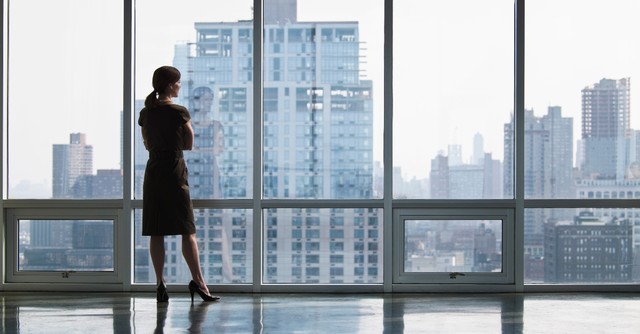 Young businesswoman standing in an office looking out over the city