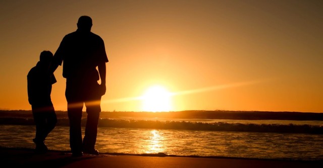 Silhouette of a dad and son on the beach at sunset