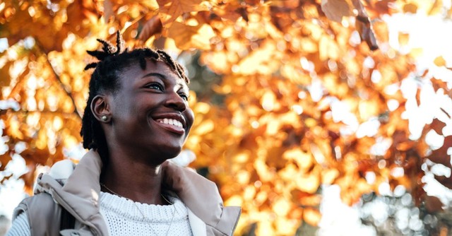 A woman smiling with fall leaves behind her