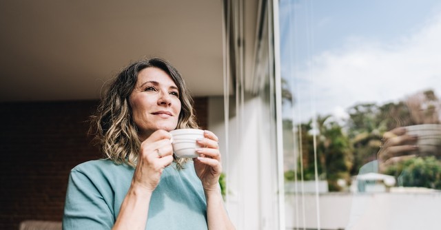 smiling woman drinking coffee in the morning looking out window