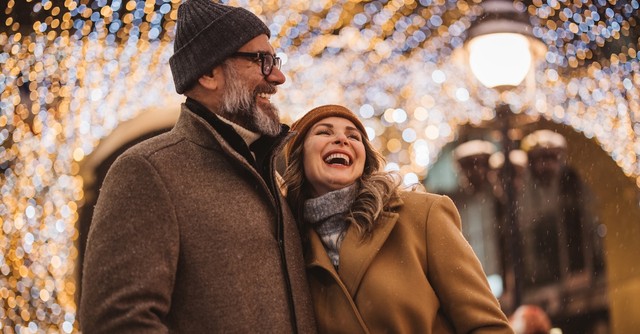 Couple walking outside under Christmas lights laughing and smiling