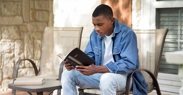 Young man reading his Bible out on a porch