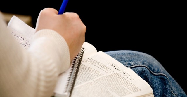 A person journaling over their open Bible, turned to Colossians