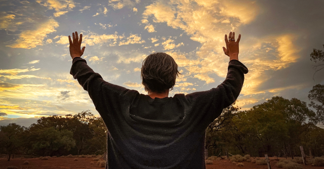 Man with hands lifted in prayer towards the sunset