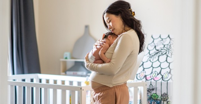 Postpartum mom holding newborn baby in nursery crib