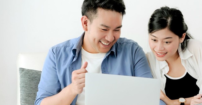 asian couple smiling together and looking into laptop screen