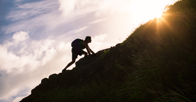 silhouette of a man climbing a hill toward the sun
