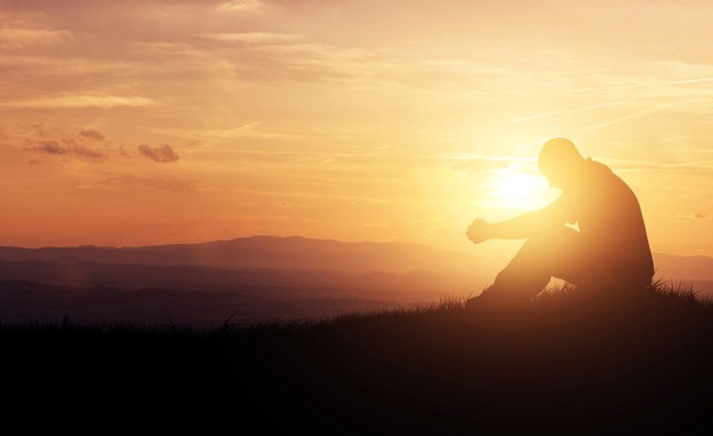 sunset silhouette of man sitting with head bowed, praying