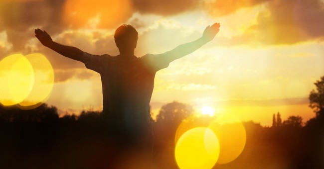 backview of man with arms outstretched in praise in golden sunrise