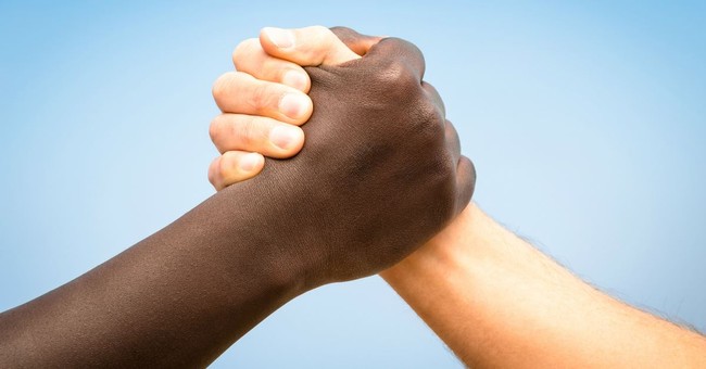 hand and forearm of a black and white person grasping hands together