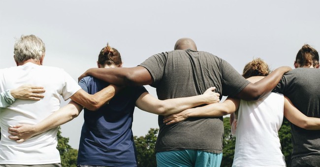 back view of diverse group of adults linking arms around waists, walking forward together