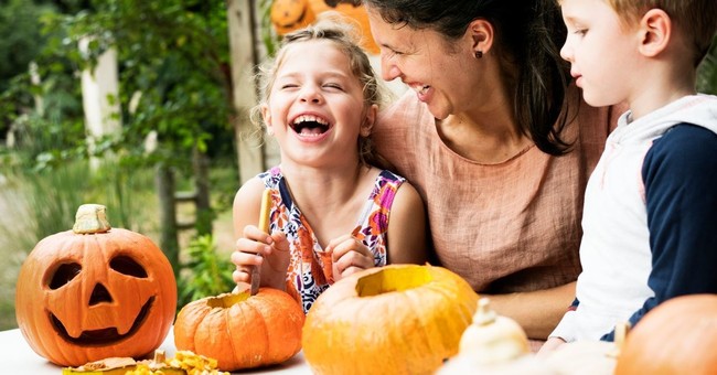 Children and their mother laugh as they carve pumpkins for Halloween