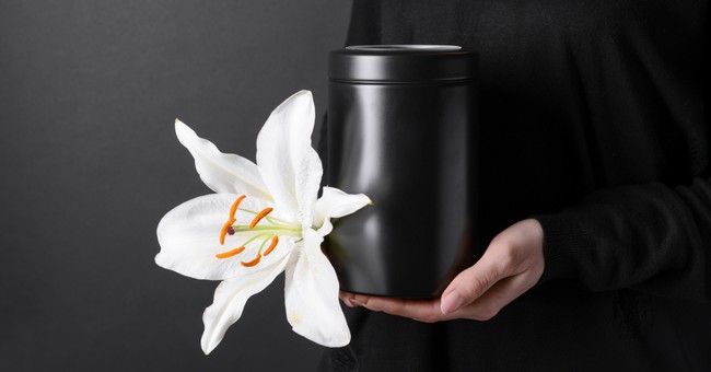 woman holding cremation urn with white lily flower on dark background