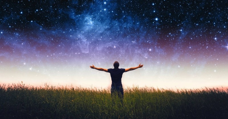 A man lifts his arms to the heavens under a starry sky - book of revelation explained