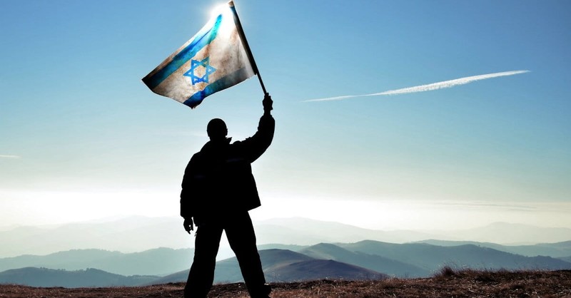 Silhouette of man waving Israel flag on mountain top