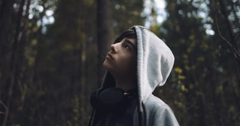 young boy teen looking up in forest wearing hoodie
