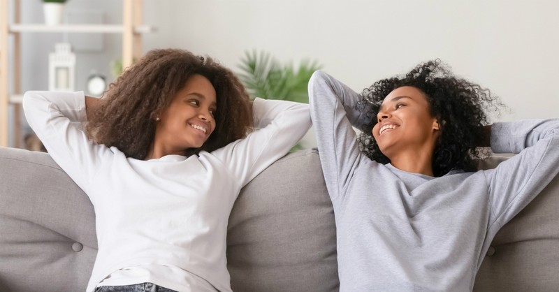 mom and teen daughter sitting on couch smiling