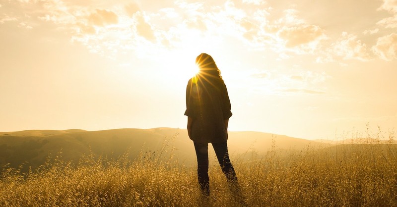 woman standing in a field at sunrise