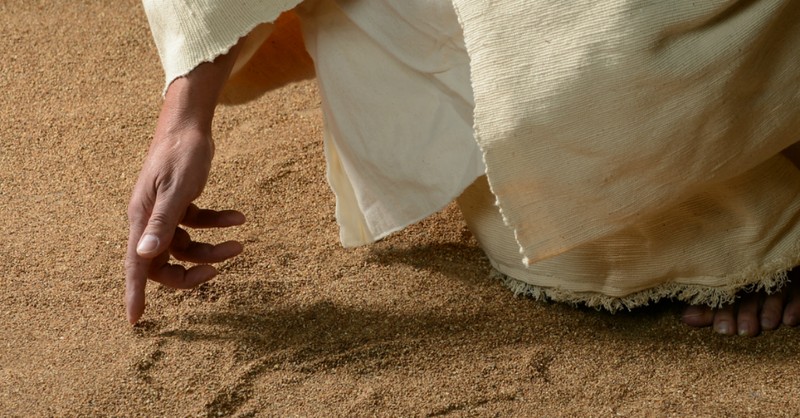 close up of jesus drawing in the sand