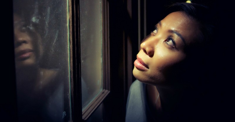 Woman looking expectantly up at the sky through a window