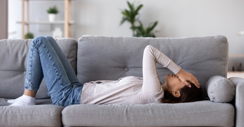 woman lying on couch with hands over her face, stressed