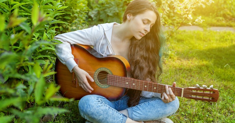 girl playing guitar by bush on lawn sunshine
