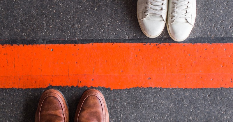 Two sets of shoes on either side of a red line on the pavement